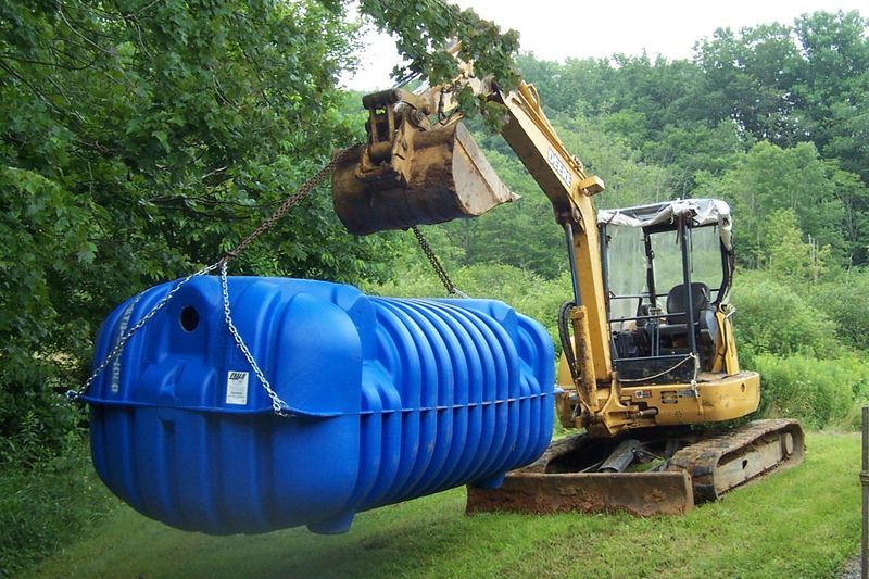 Excavator lowering a blue polyethylene septic tank